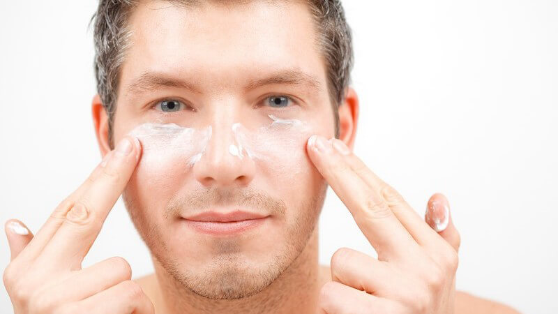 Mann trägt Creme auf Gesicht unter Augen auf