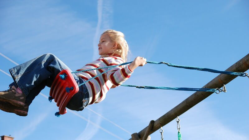 Kleines Mädchen beim Schaukeln unter blauem Himmel