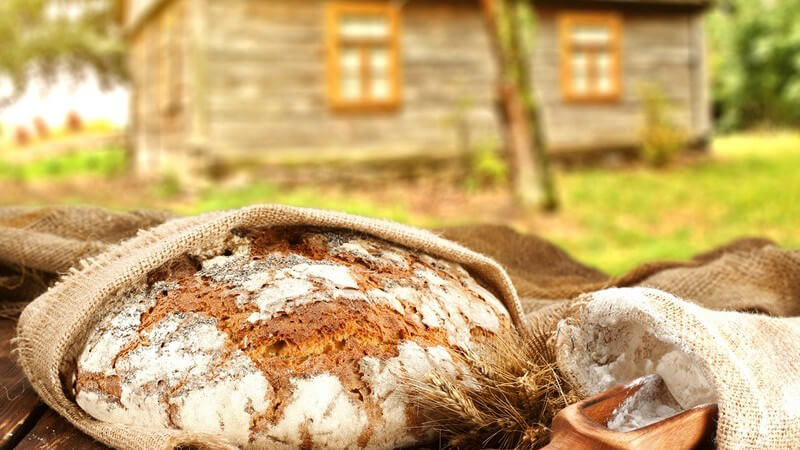 Frisches Landbrot eingewickelt in Jutestoff auf rustikalem Holztisch vor einem Holzhaus