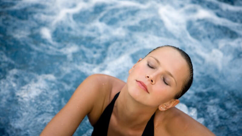 Ansicht von oben: Junge Frau mit geschlossenen Augen im Whirlpool