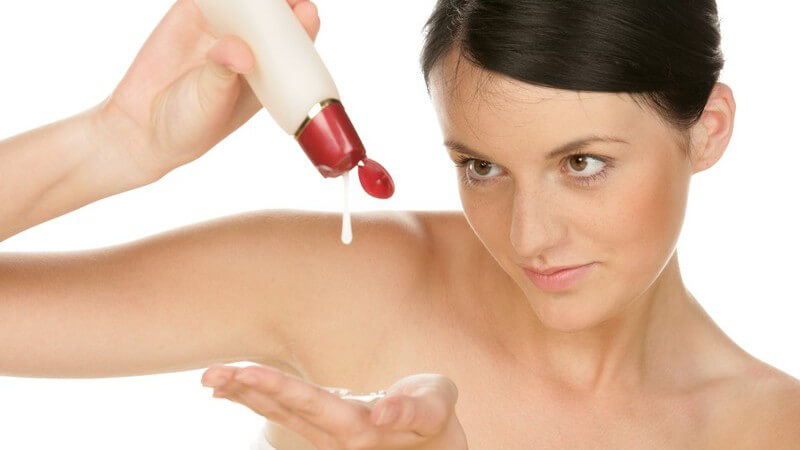 Junge Frau trägt Lotion auf Hände auf, weißer Hintergrund