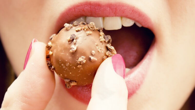 Frau mit roten Lippen und Fingernägeln nascht eine runde Schokopraline