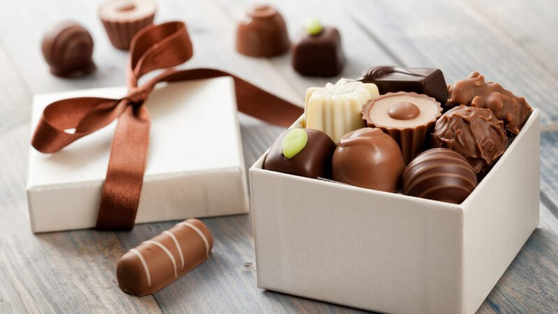 Pralinen in einer weißen Schachtel, daneben der Deckel mit brauner Schleife