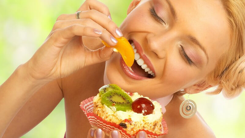 Blonde, lächelnde Frau isst mit geschlossenen Augen einen Früchtekuchen