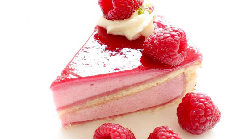 Stück Himbeer-Sahnetorte, daneben frische Himbeeren