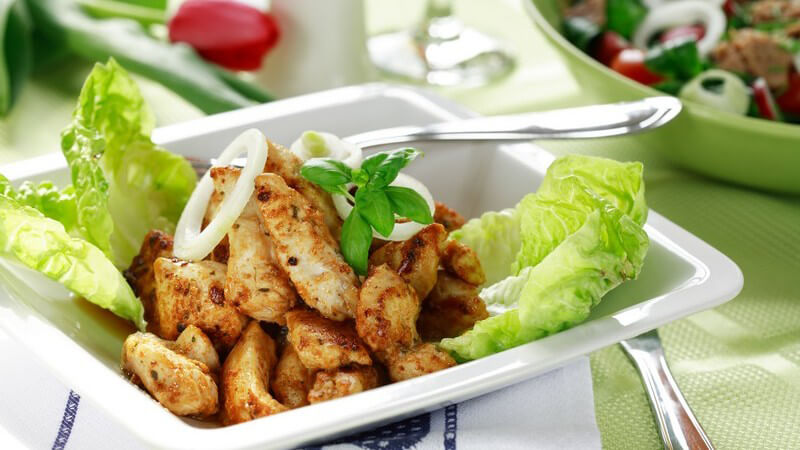 Gebratene Hähnchenstreifen mit Salat auf weißer, eckiger Schale