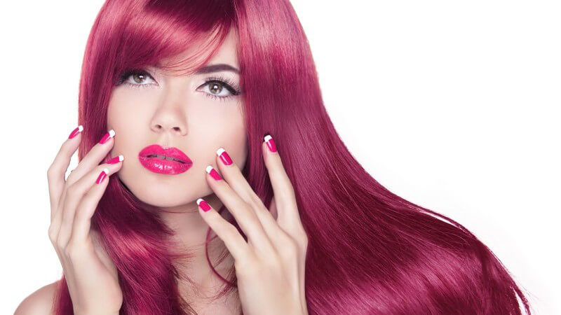 Portrait einer Frau mit langen glänzenden pink-gefärbten Haaren, Lippenstift und Nagellack