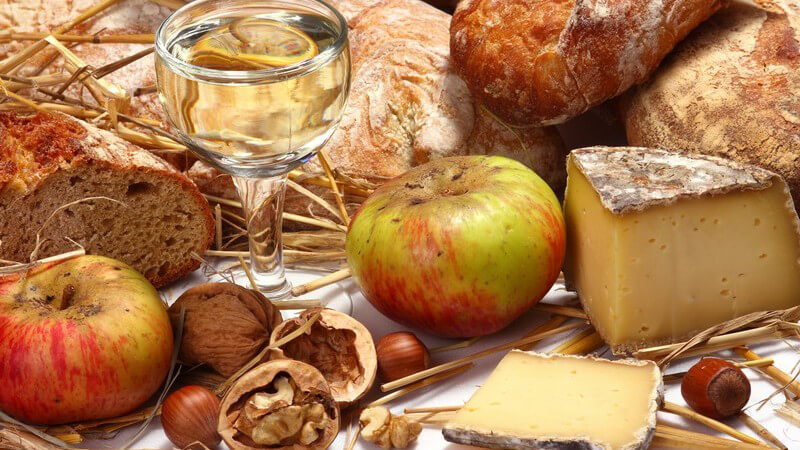 Frisches Brot, Äpfel, Weißwein und Käse auf weißer Decke mit Stroh