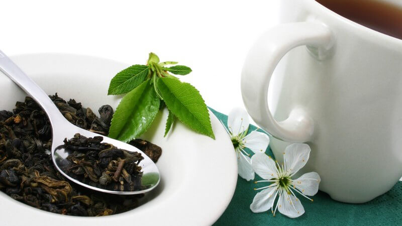 Becher mit Tee, daneben Teller mit getrockneten Teeblättern auf Löffel