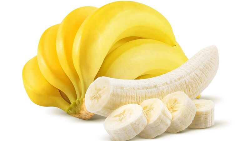 Bund Bananen neben geschälter und gestückelter Banane vor weißem Hintergrund
