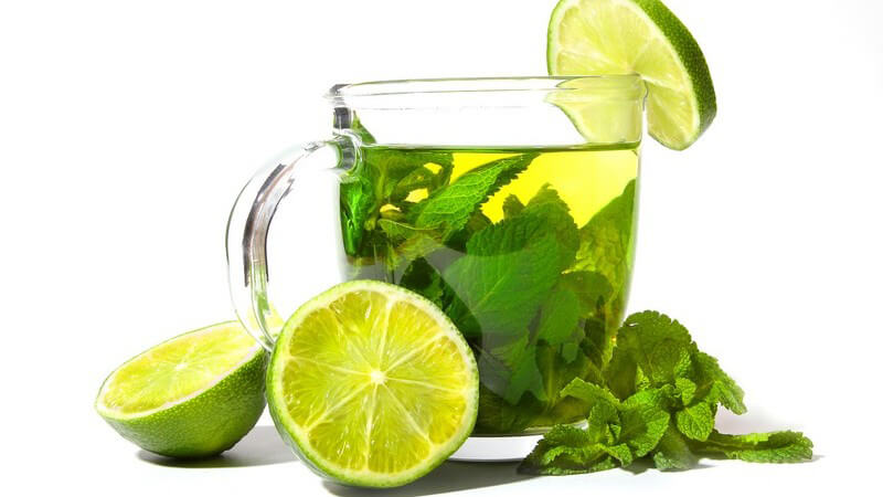 Glas Tee mit Pfefferminzblättern, darum Zitronenscheiben und -hälften