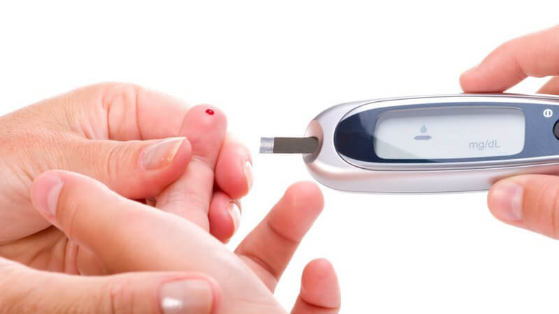 Eine Hand hält eine andere mit Blutstropfen an Fingerkuppe für Glucoseschnelltest o. Blutzuckertest für Diabetiker