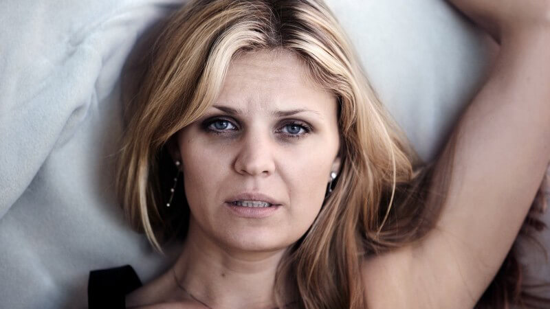 Frau liegt im Bett, müde, hat Augenringe, Schlafstörungen