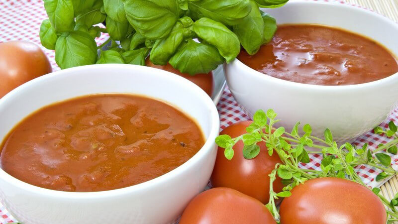 Tomatensuppe in Schalen zwischen frischen Tomaten und Basilikum