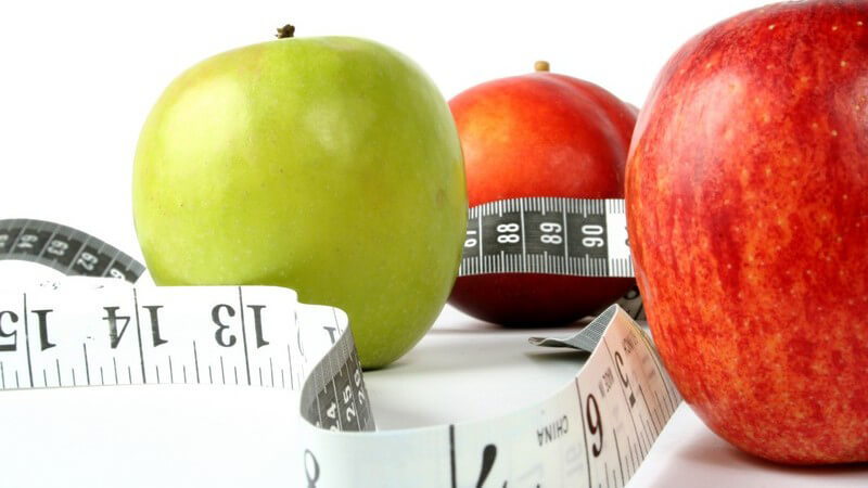 Grüne und rote Äpfel mit Maßband auf weißem Hintergrund