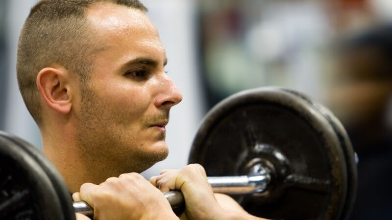 Gewichtheber mit angespanntem Gesicht und Langhantel vor der Brust