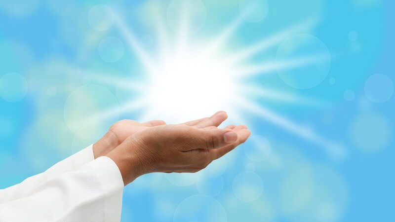 Offene, betende Hände unter der Sonne bei blauem Himmel