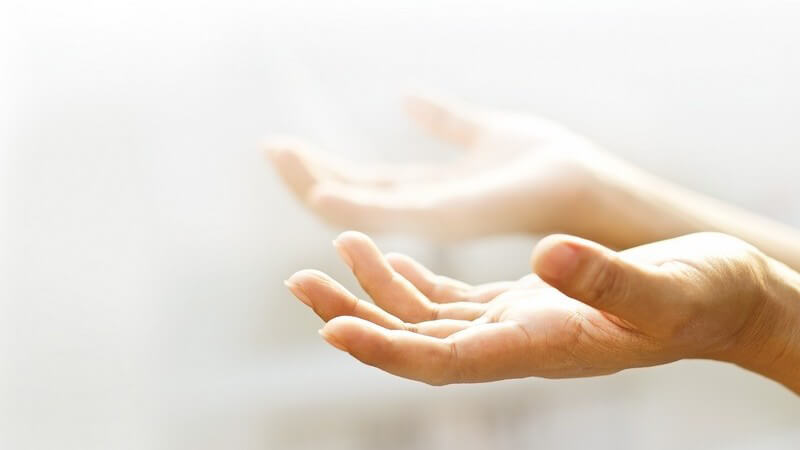 Zwei offene Hände mit der leeren Handinnenfläche nach oben, umgeben von leichtem Nebel und Licht