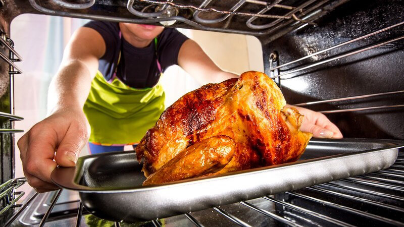 Mann schiebt Hähnchen oder Truthahn Braten in den Backofen