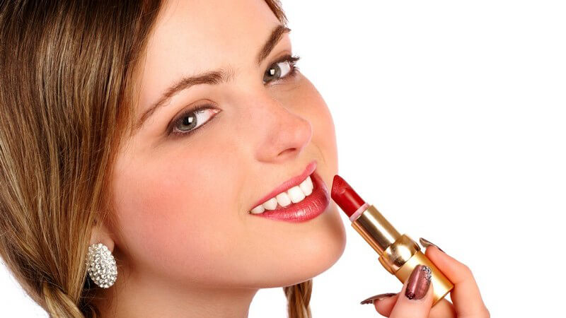 Blondes Mädchen mit weißem Ohrring hält roten Lippenstift an ihren Mund