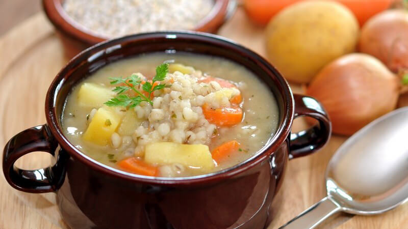 Graupeneintopf, Suppe mit Perlgraupen in Schüssel, daneben die Zutaten auf Holzbrett