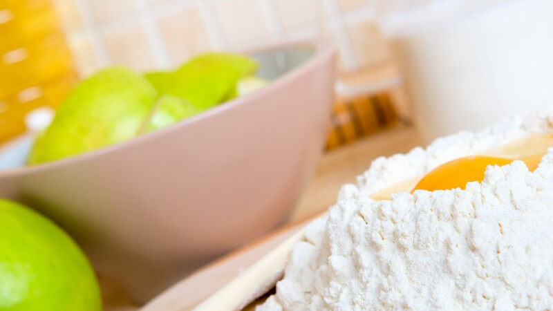 Rohes Ei auf Mehl, daneben Schüssel mit grünen Äpfeln