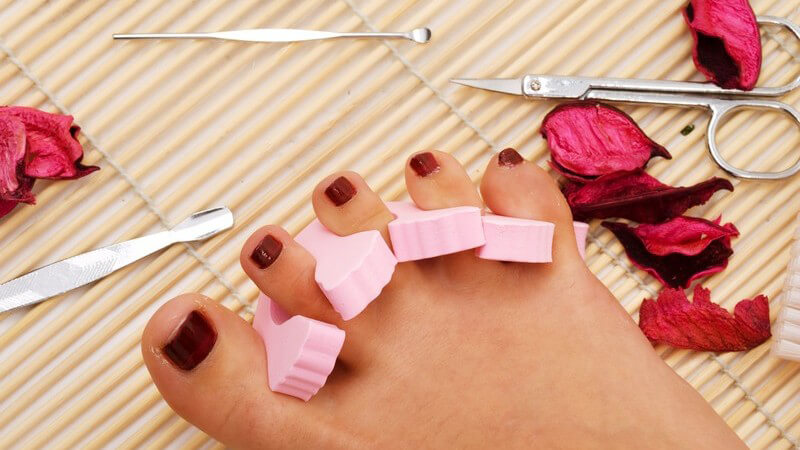 Fuß mit lackierten Zehennägeln und rosa Zehenabstandshaltern