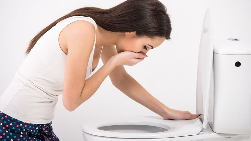 Junge Frau vor einer Kloschüssel, eine Hand vor den Mund gehalten