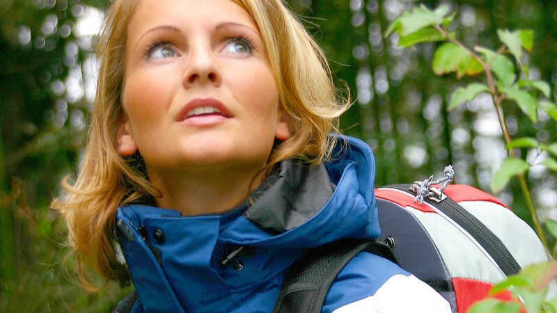 Frau mit Jacke und Rucksack im Wald beim Wandern