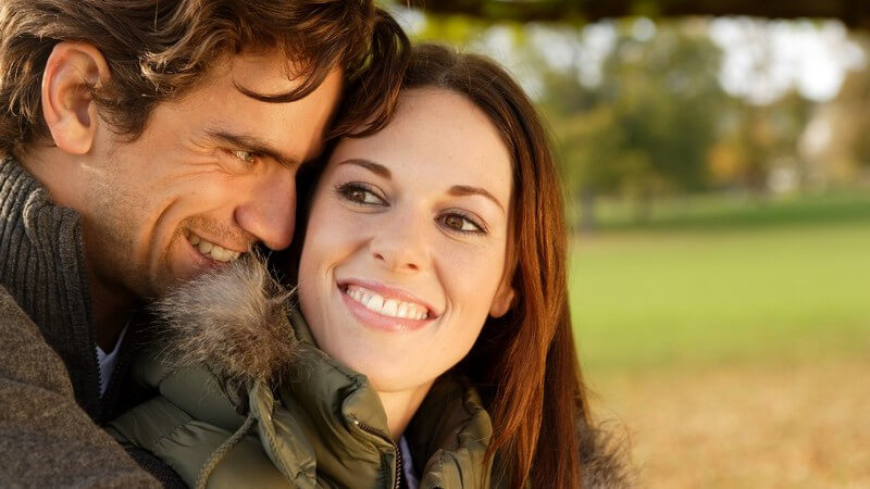 Junges Paar im Herbst im Park, er umarmt sie von hinten