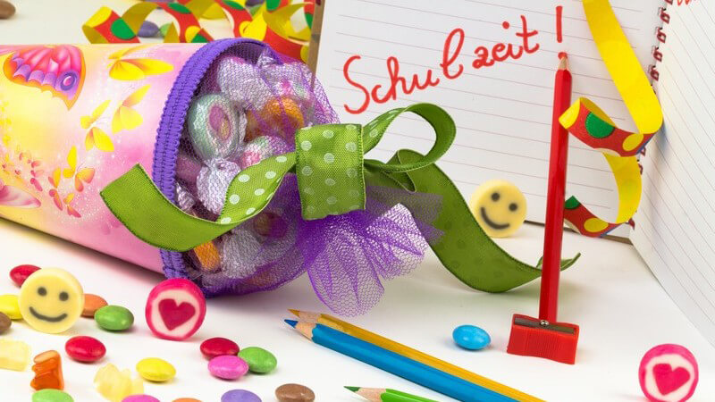 Einschulung, erster Schultag: Schultüte mit Süßigkeiten, drumherum bunte Stifte