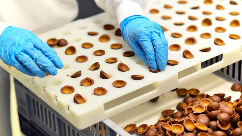 Fabrikarbeiter mit blauen Handschuhen bei der Herstellung von Pralinen