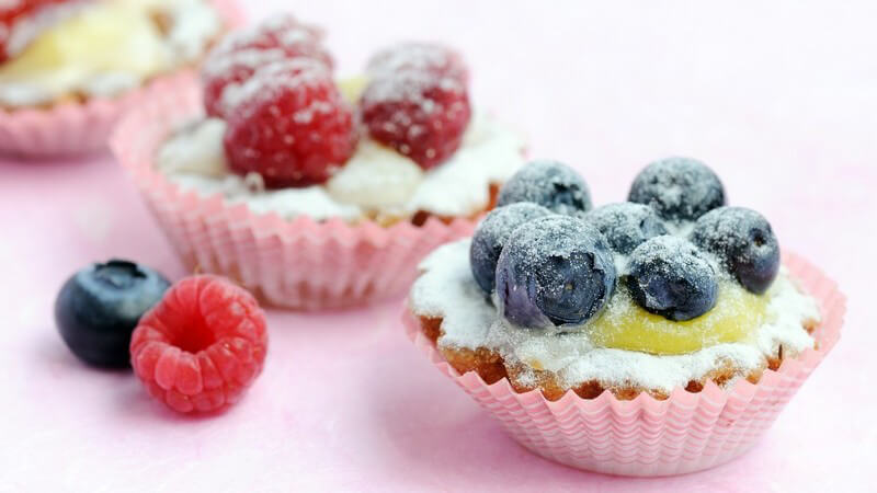 Kuchenteilchen mit frischen Früchten und Zuckerguss auf weißem Hintergrund