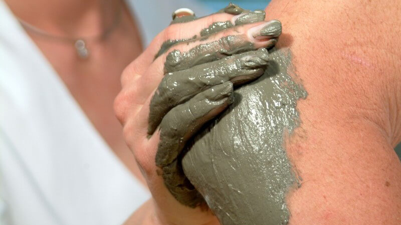 Frau in weißer Kleidung trägt Schlamm auf einen Ellenbogen auf