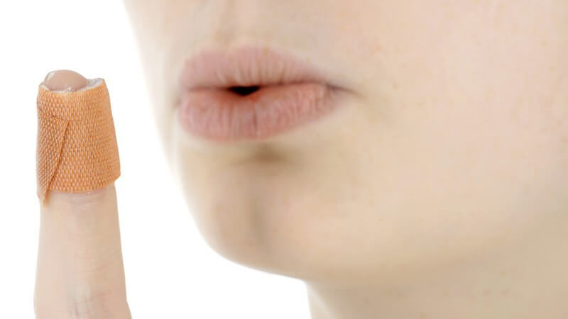 Frau pustet auf ihren verletzten Finger mit Pflaster