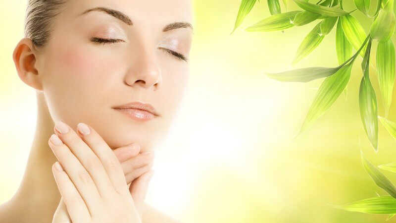 Schöne Frau mit geschlossenen Augen vor einem leuchtend grünen Hintergrund fasst sich mit den Händen ans Kinn