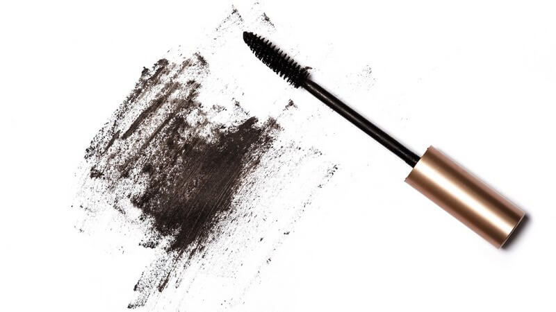 Mascara-Bürstchen und schwarze verwischte Schminke auf weißem Untergrund