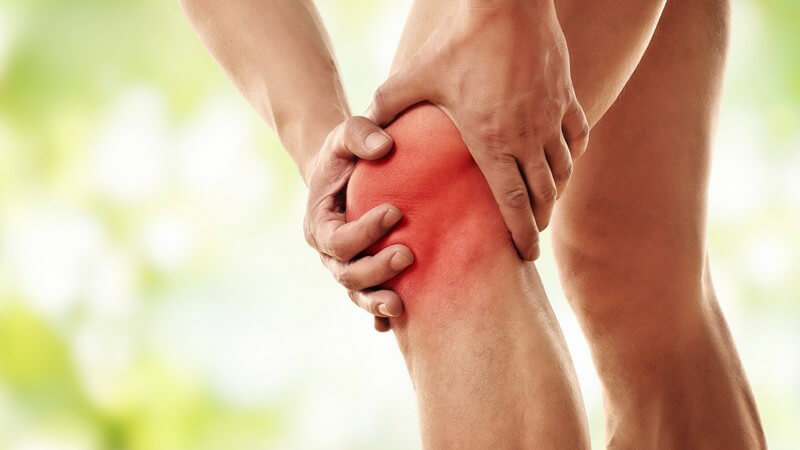 Mann greift sich vor Schmerzen ans linke Knie, Knieschmerzen rot hervorgehoben