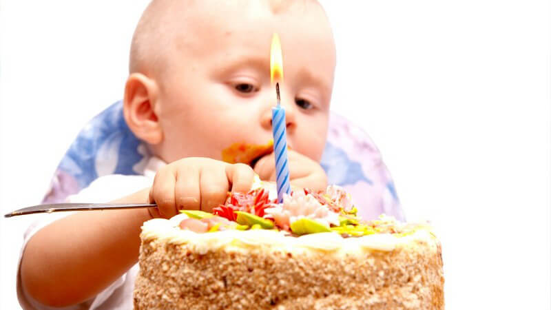 Baby o Säugling sitzt in Hochstuhl vor Geburtstagskuchen mit Kerze und isst davon