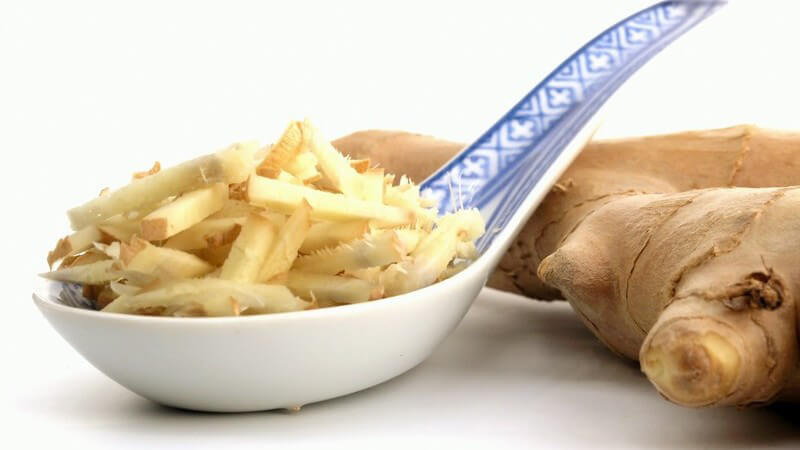 Kleingeschnittener Ingwer in Löffel, daneben ganze Ingwerwurzel