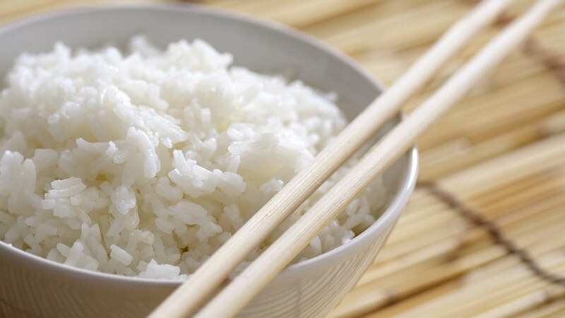 Nahaufnahme Schüssel mit Reis und Stäbchen auf Bastset