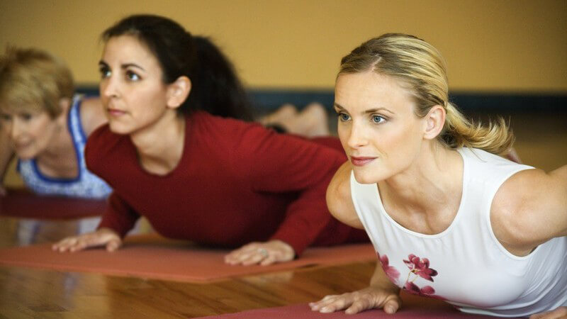 Blonde und dahinter brünette Frau stützen sich auf Yogamatten hoch