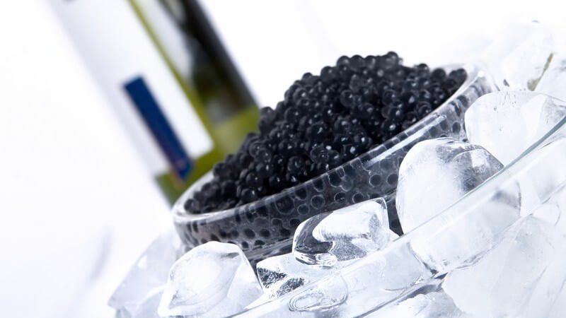 Schwarzer Kaviar in Glasschale eisgekühlt, im Hintergrund Weinflasche