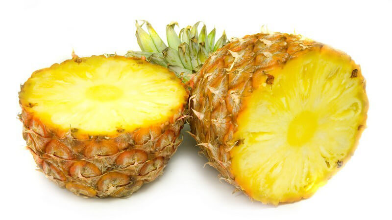 Halbierte Ananas mit grünem Strunk auf weißem Untergrund