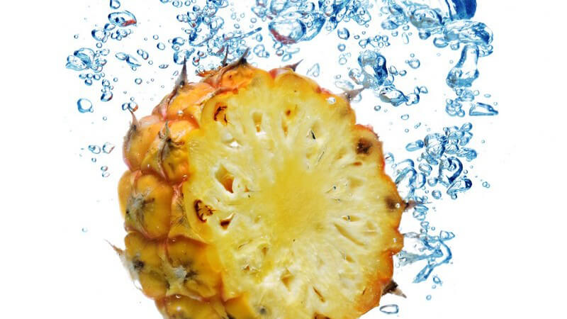 Aufgeschnittene Ananas fällt ins Wasser und hinterlässt Wasserblasen unter Oberfläche