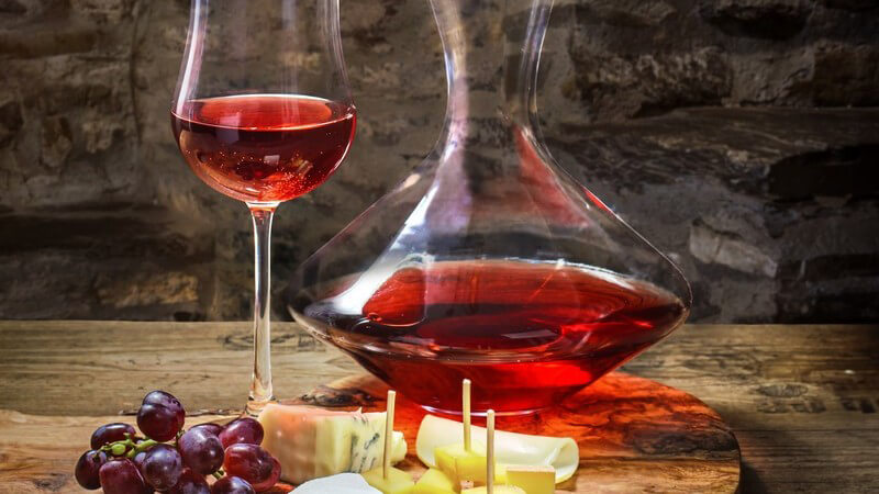 Holzbrett mit Rotwein, Trauben und Käse im urigen Keller