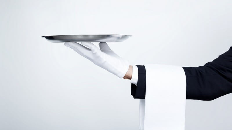 Weiße Serviette hängt über dem Unterarm eines Kellners mit weißem Handschuh, hält leeres Silbertablett