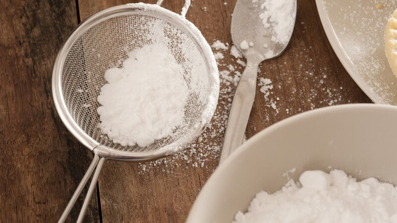 Kleines Küchensieb mit Puderzucker auf dunklem Holztisch