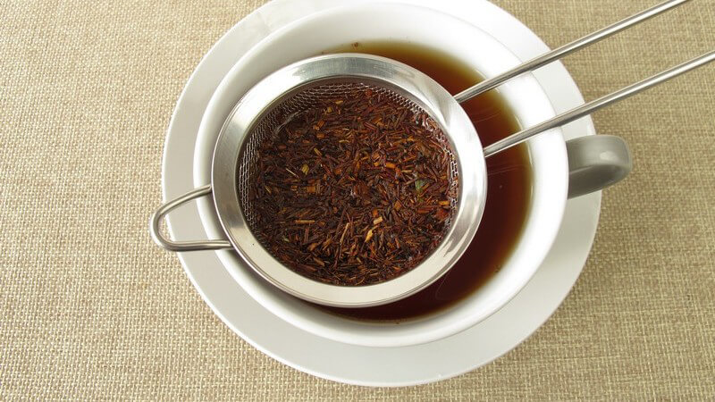 Teesieb mit Rotbuschtee liegt auf einer Tasse