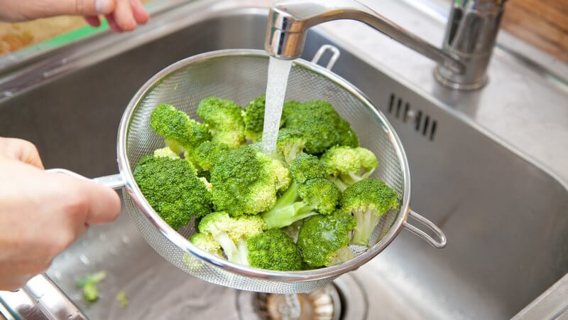 Brokkoliröschen werden in Abtropfsieb unter fließendem Wasser gewaschen
